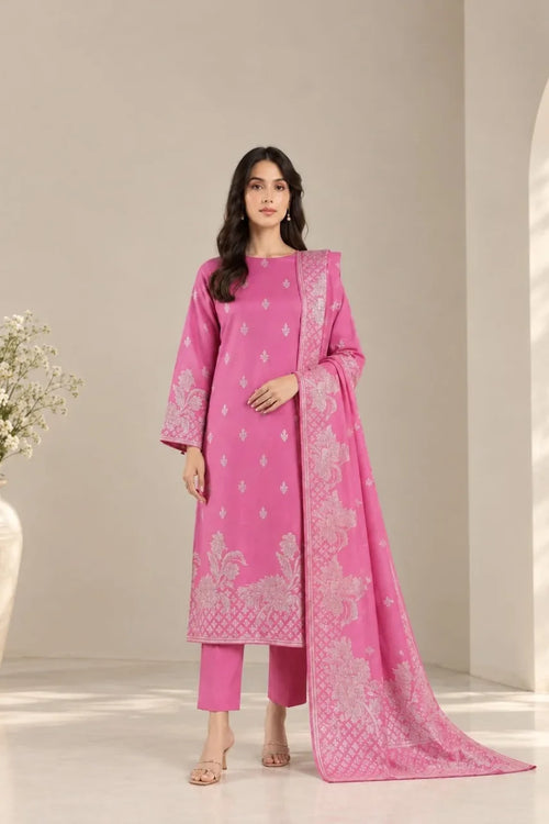 A woman models a bright pink three-piece traditional outfit with matching pants and a long dupatta, featuring light pink floral embroidery, set against a neutral beige studio background.