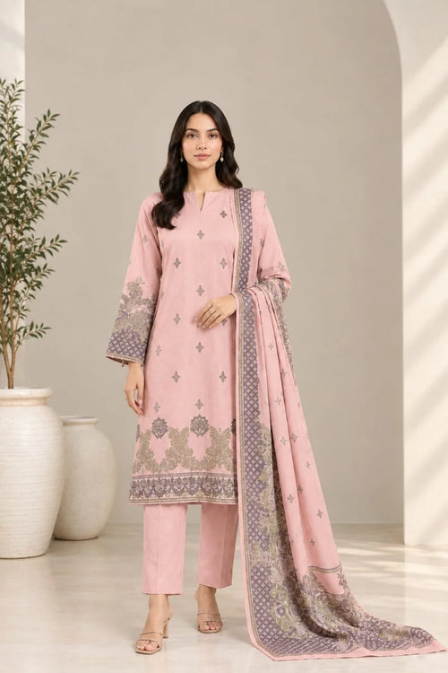 A woman modeling a light pink three-piece ethnic suit with matching trousers and a long dupatta featuring lavender and gold floral patterns, set against a neutral beige background with decorative white vases.