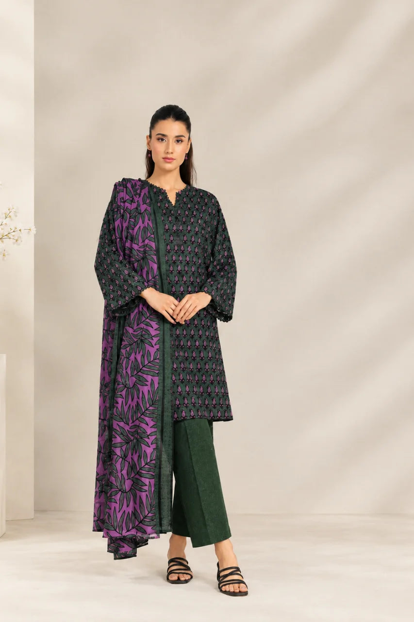 A woman modeling a traditional three-piece outfit consisting of a black kurta with purple and gold floral patterns, a matching purple dupatta, and dark green pants, set against a neutral beige studio backdrop.