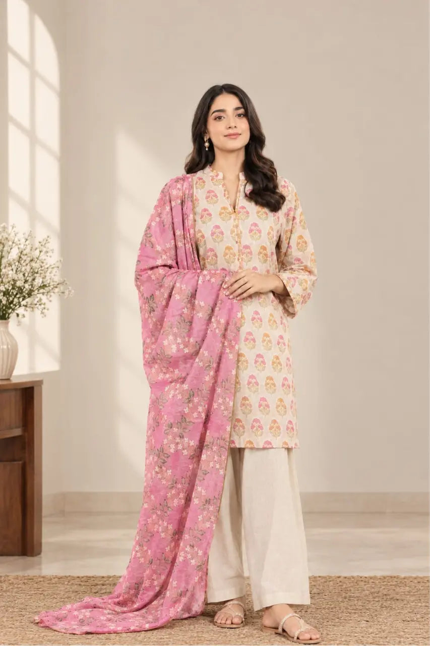 A woman models a traditional salwar kameez suit set featuring a cream-colored kurta with pink and gold floral prints, cream-colored palazzo pants, and a pink dupatta with gold floral motifs, set against a warm beige background.