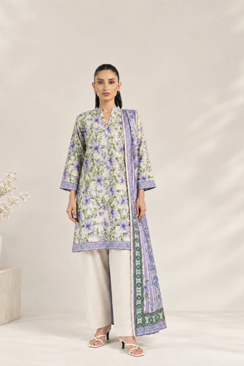 A woman models a three-piece traditional outfit featuring a light green kurta with purple and green floral patterns, paired with light beige wide-leg trousers and a matching purple patterned dupatta, set against a neutral beige background.