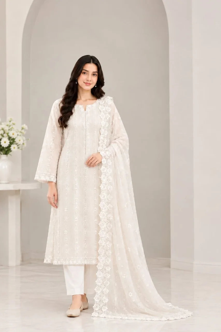 A woman modeling a traditional white Indian salwar kameez suit with a matching embroidered dupatta, set against a minimalist light gray arched studio backdrop.