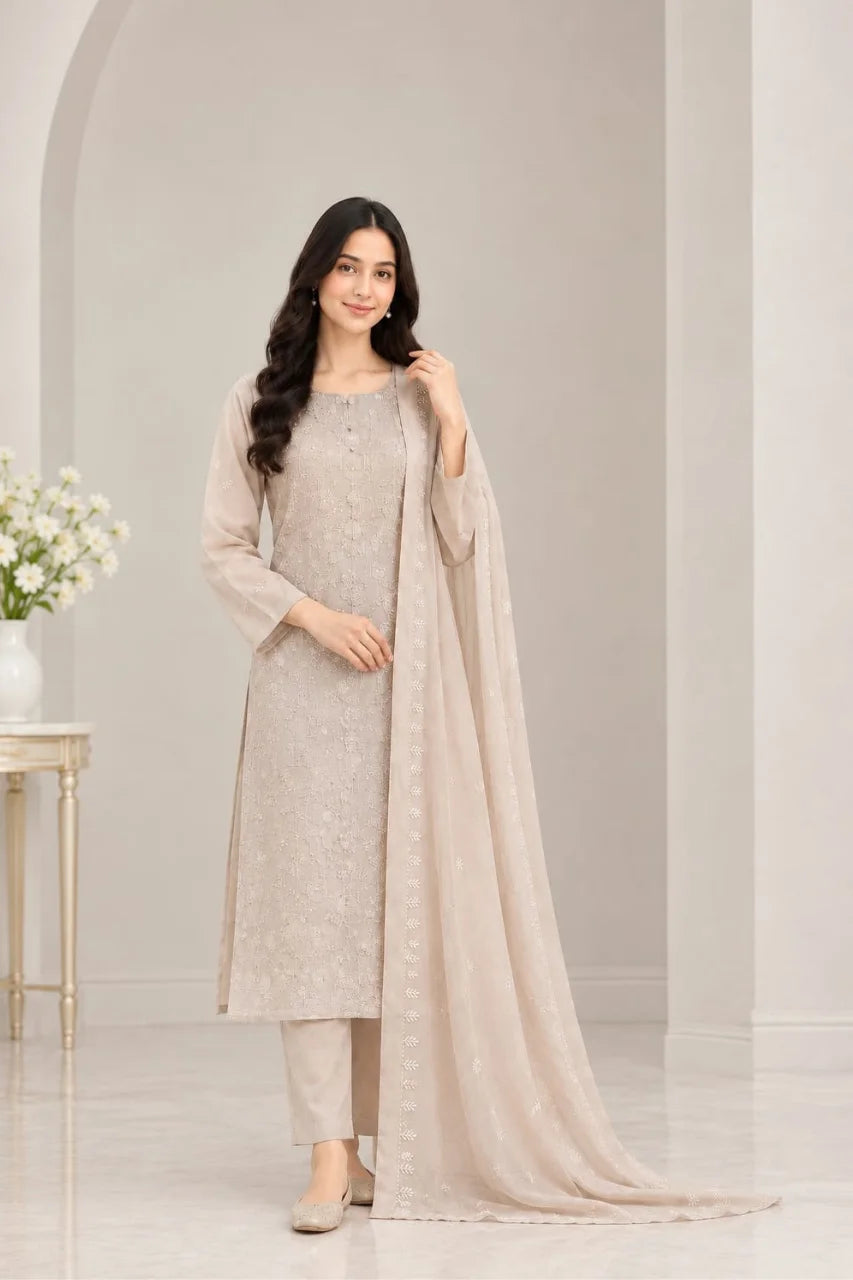 A woman modeling a light beige traditional South Asian salwar kameez suit with matching pants and a sheer dupatta, set against a minimalist beige interior background.