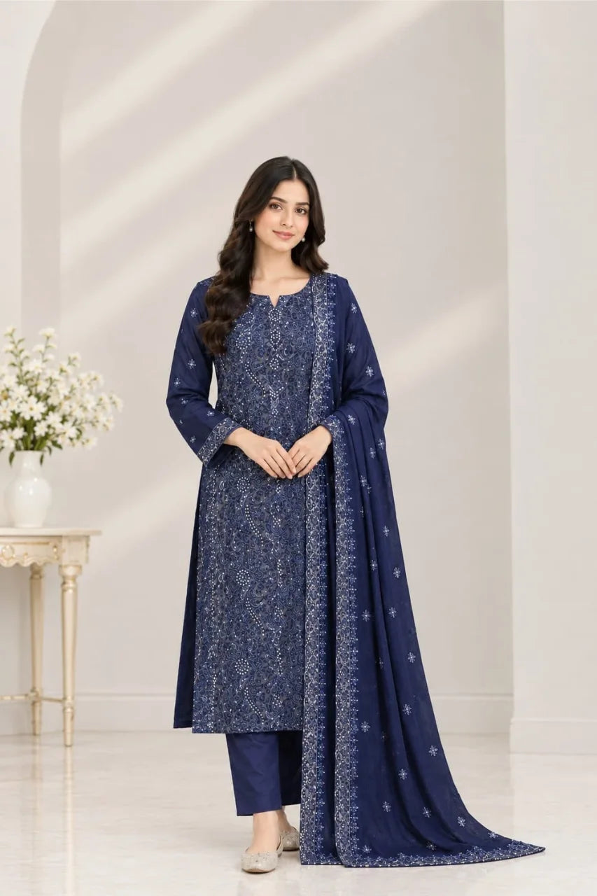 A woman modeling a navy blue chiffon salwar kameez suit with intricate silver floral embroidery, featuring a matching dupatta, set against a bright, minimalist interior background.