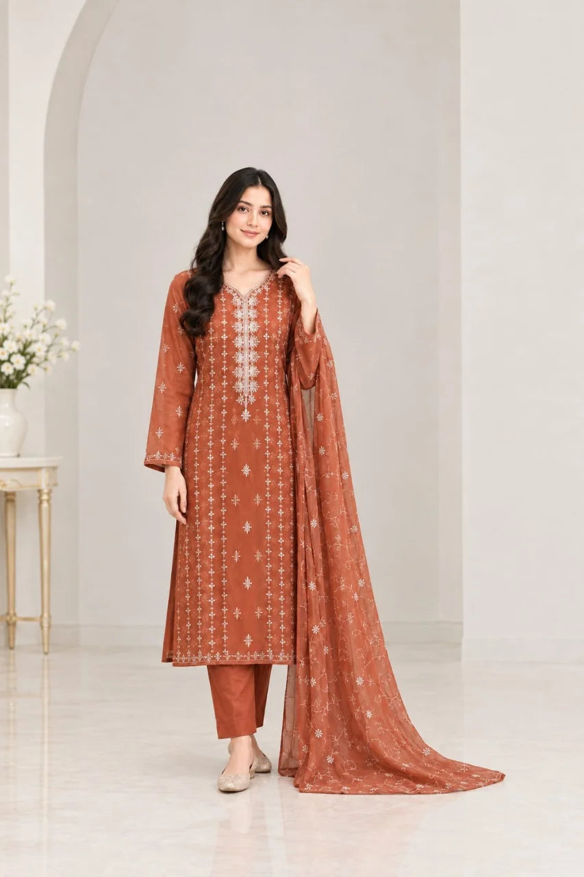 A woman models a rust-orange salwar kameez suit with white embroidery and a matching dupatta in a bright, modern studio setting.