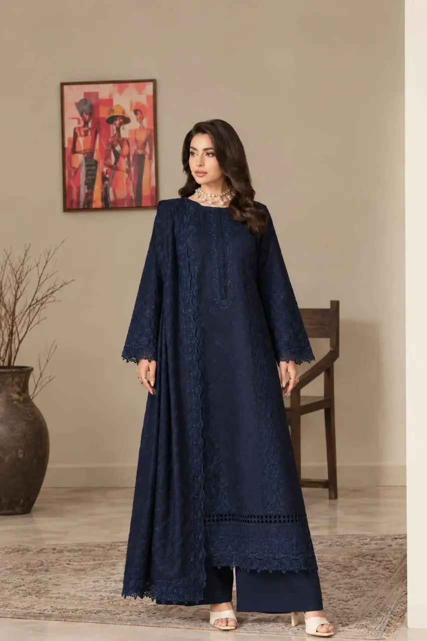 A woman models a long navy blue embroidered kurta with matching wide-leg trousers in a styled indoor setting with a beige wall, framed art, and a wooden chair.